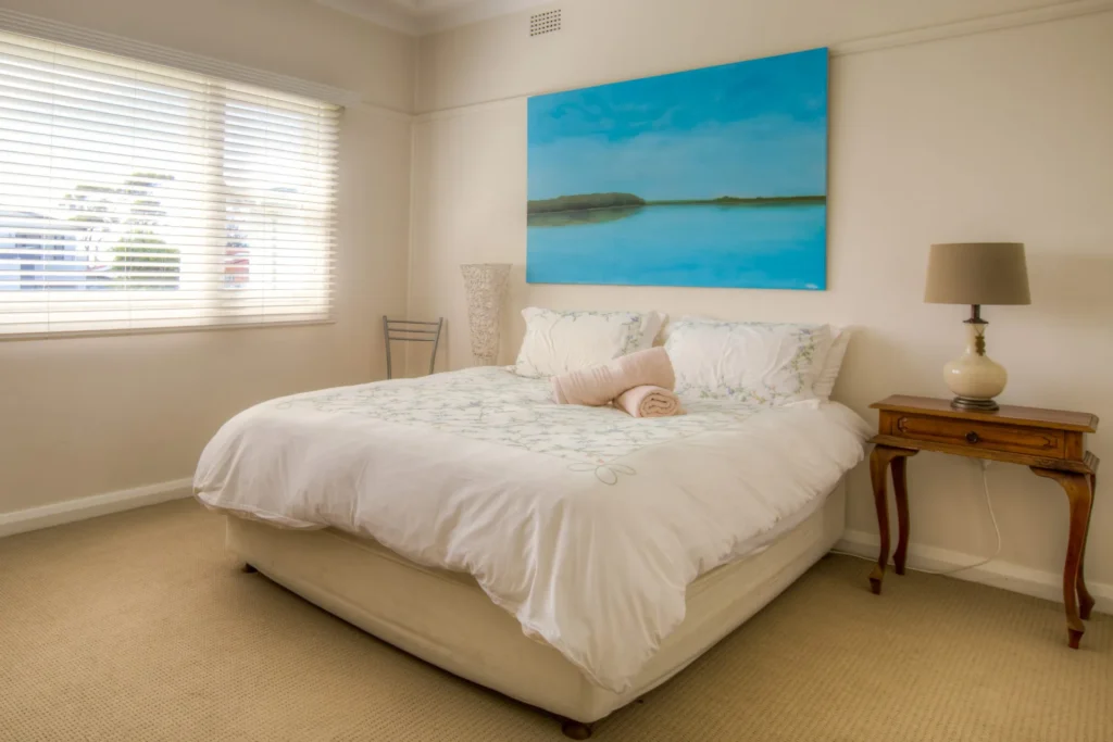Bright bedroom with a blue ocean painting at Fibro Majestic at Hyams Beach